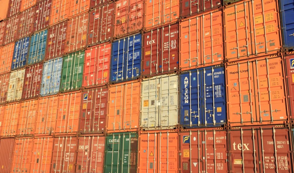 blue-white-orange-and-brown-container-van-163726 Colorful shipping containers stacked in a harbor, symbolizing global trade.
